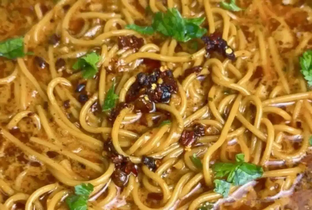A plate of caramelized onion and garlic spaghetti garnished with herbs.