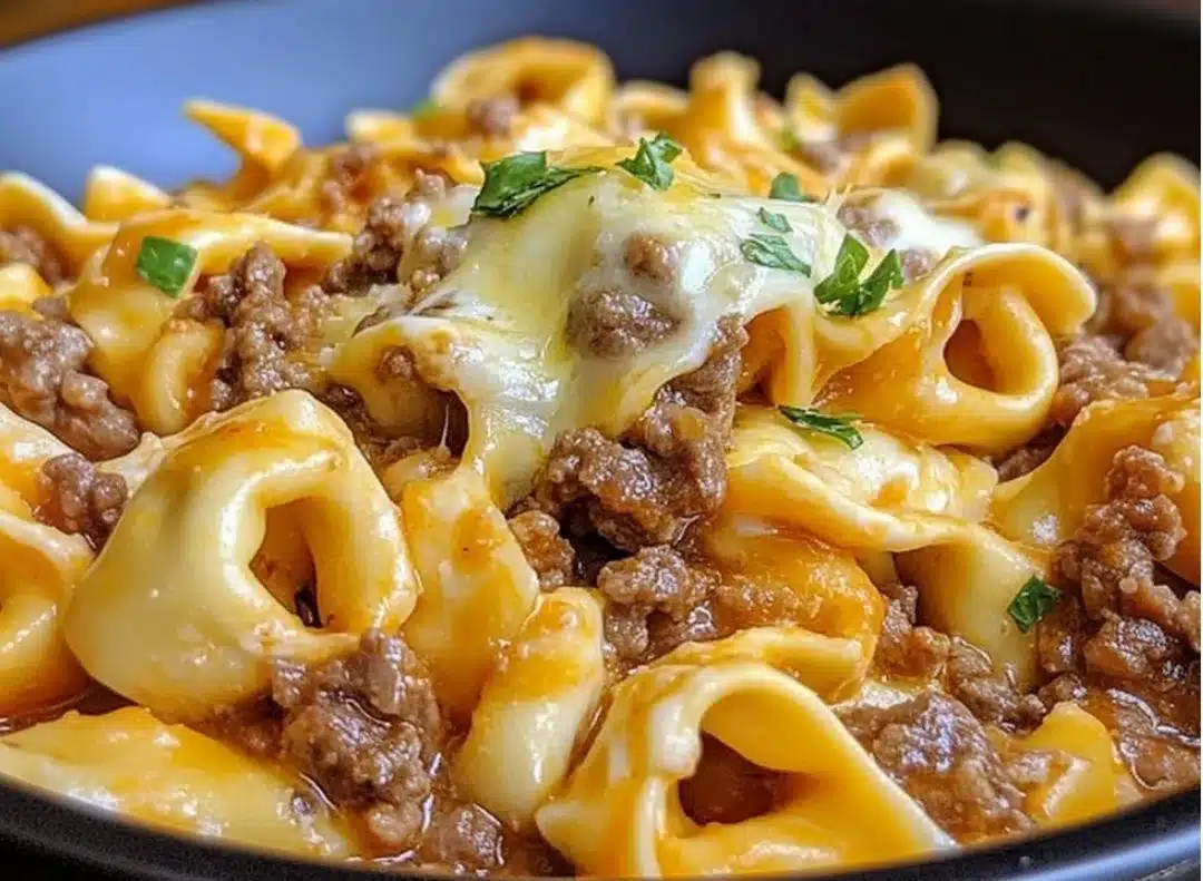Bowl of creamy cheesesteak tortellini in provolone sauce, garnished with herbs.